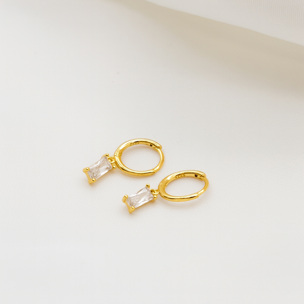 Gold hoop earrings with clear gemstones on a light beige background