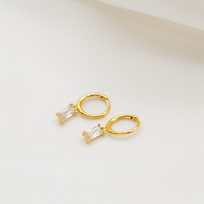 Gold hoop earrings with clear gemstones on a light beige background